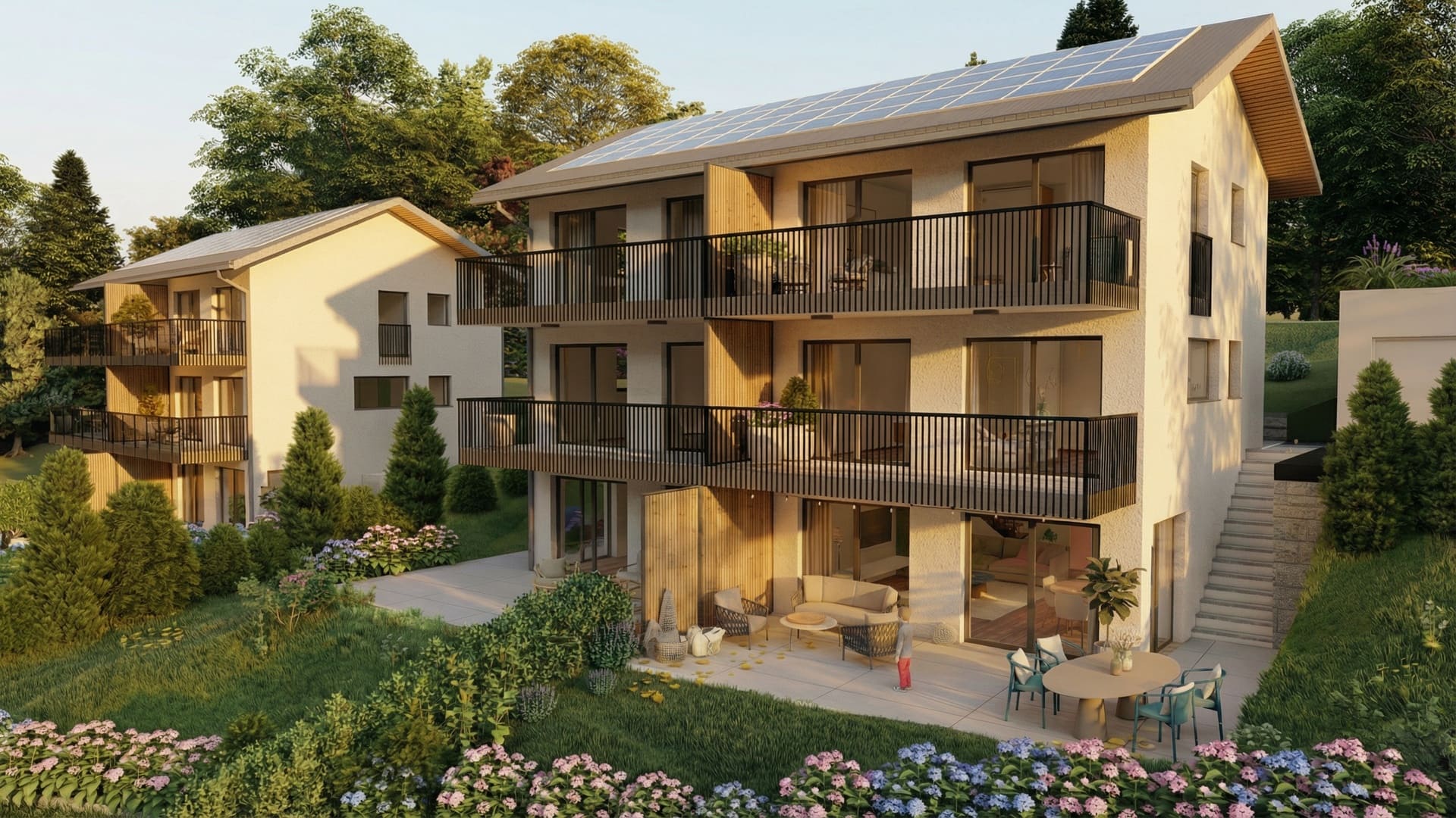 Vue extérieure de villas neuves avec façades claires, balcons en métal noir, panneaux solaires, terrasses meublées et jardin arboré baigné de lumière chaude.